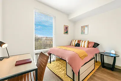 Spacious private bedroom in a student apartment featuring a large bed, desk area, and bright windows